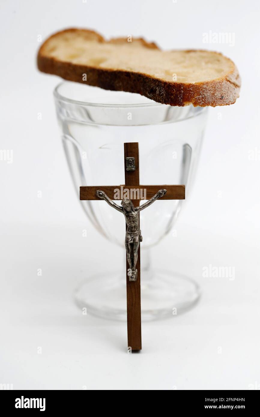 Lent starts on Ash Wednesday and ends on Holy Thursday Evening. Glass of water, christian cross and bread. France. Stock Photo