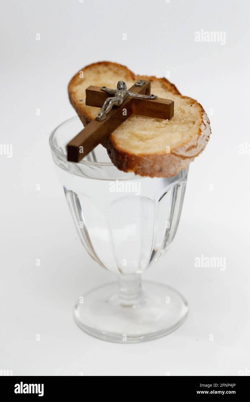 Lent starts on Ash Wednesday and ends on Holy Thursday Evening. Glass of water, christian cross and bread. France. Stock Photo
