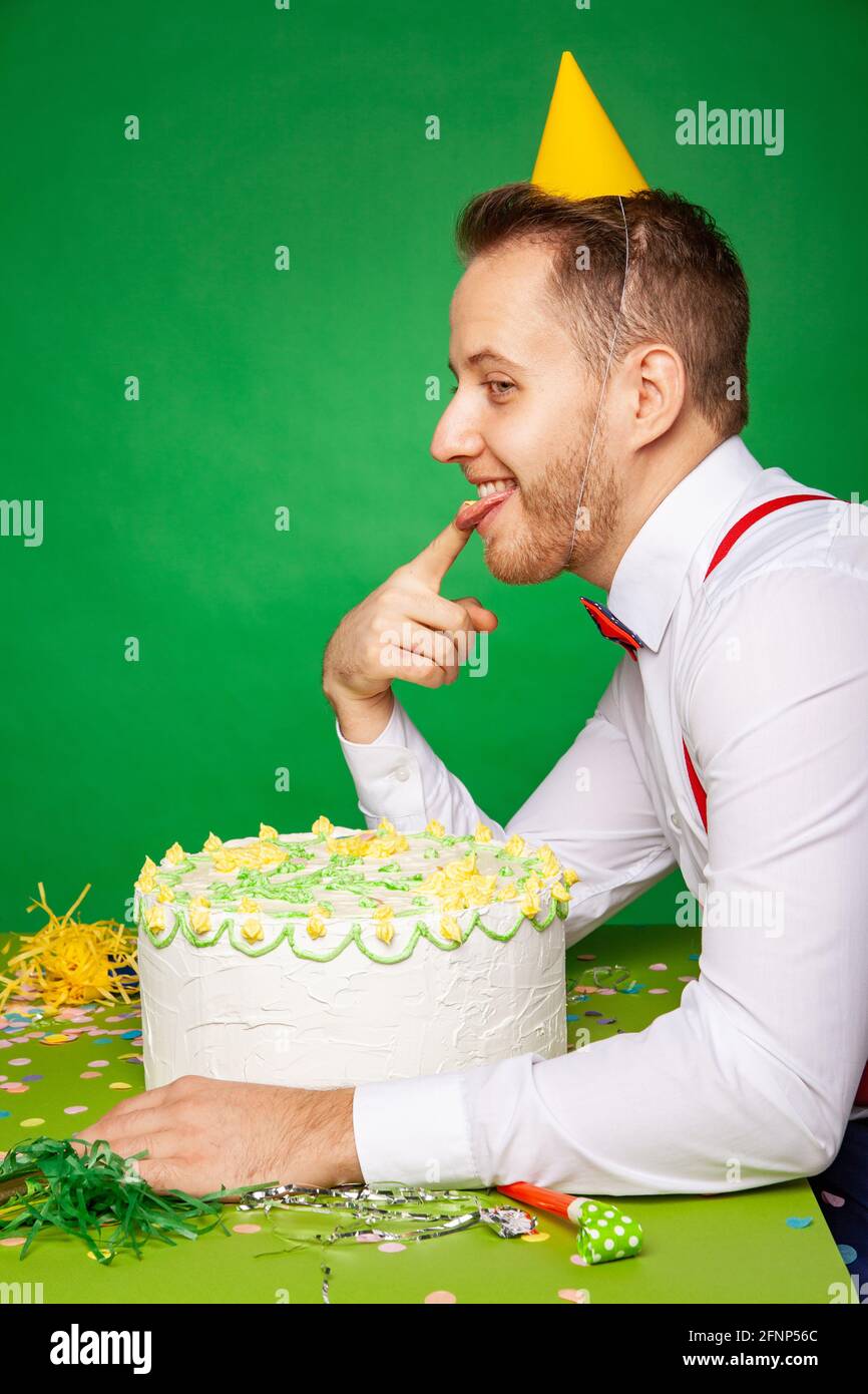 Male in party hat sitting at table and tasting sweet delicious birthday