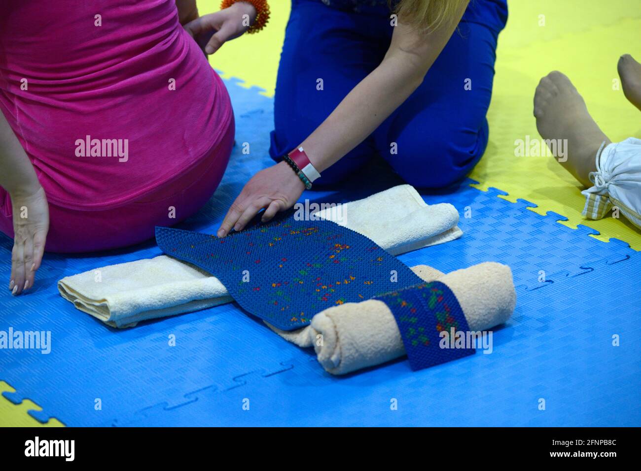 Female therapist hands help a woman to lay on Lyapko acupuncture mat