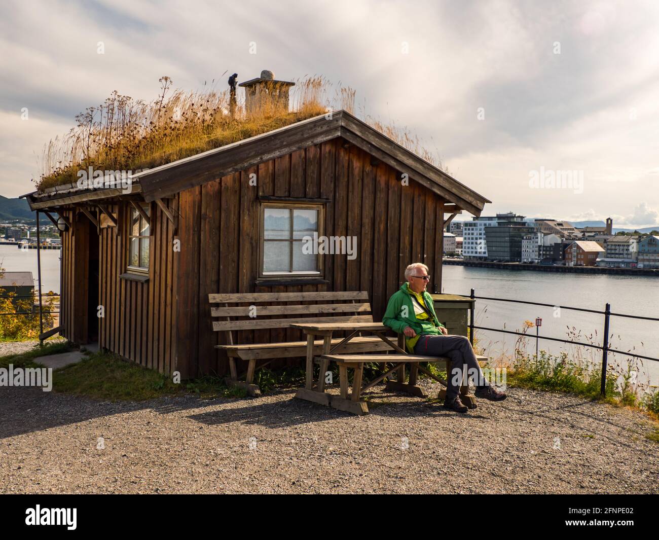 Bodo, Norway - Aug, 2019: A tourist sits on a bench in front of a typical Norwegian wooden house on Nyholmen - an area on the Burøya peninsula. Nyholm Stock Photo