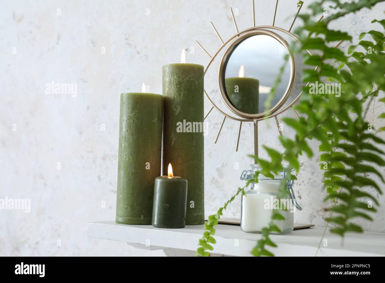 Burning candles, mirror and houseplant on shelf near light wall Stock