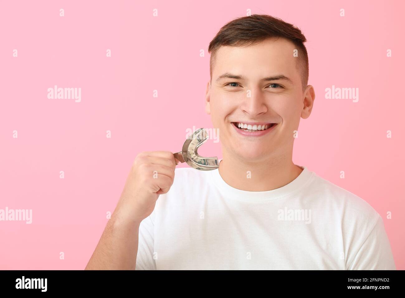 Young man with dental tool for making mold of teeth on color background