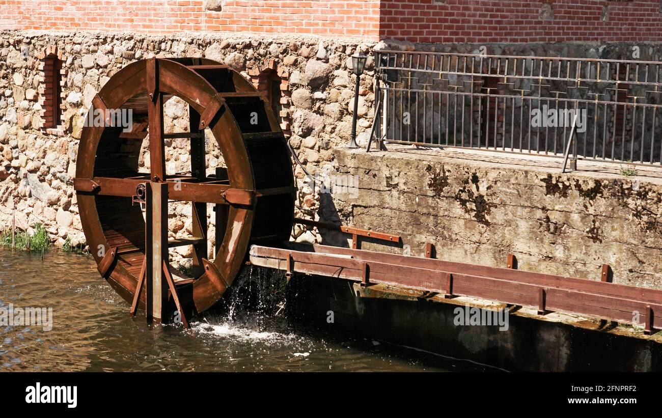 An old water mill on the background of a brick building. Wooden mill