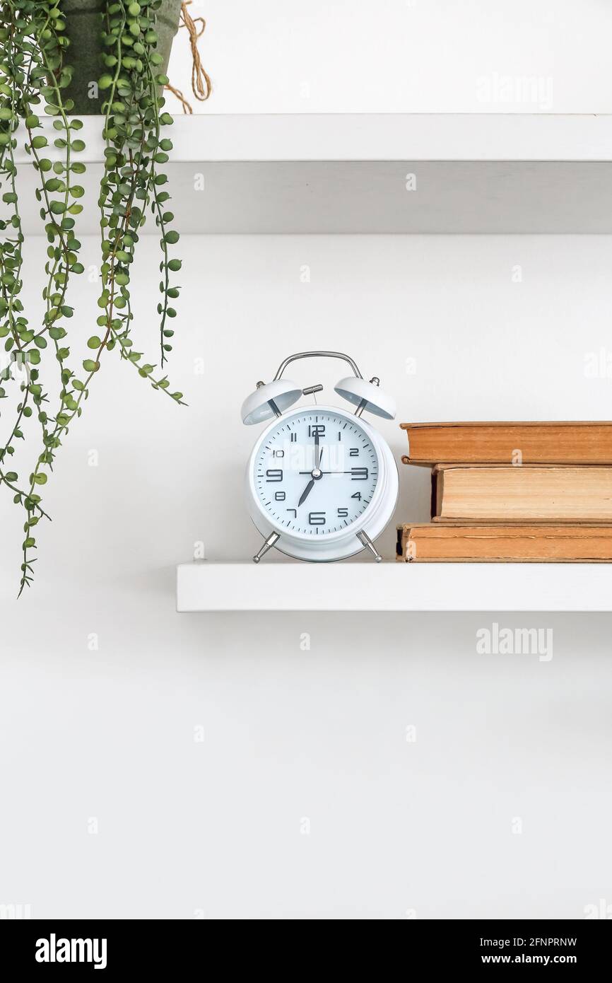 Book shelves with alarm clock hanging on light wall Stock Photo Alamy
