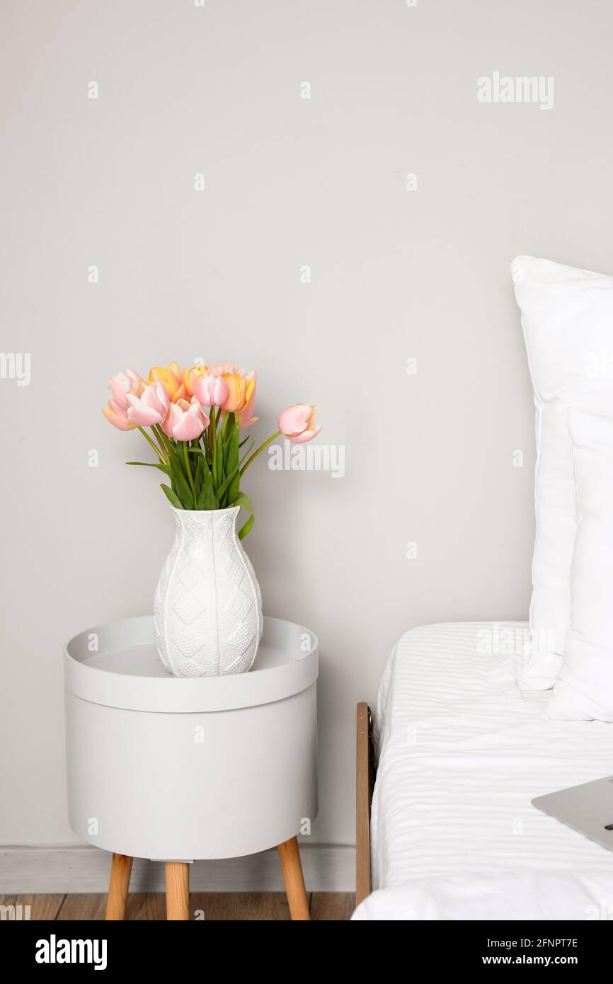 Tulip flowers on bedside table near white wall in room Stock Photo