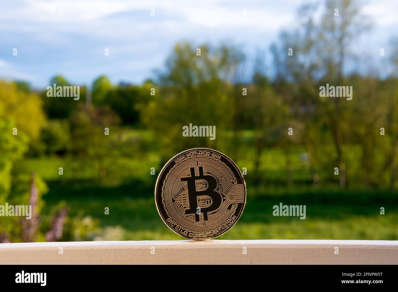 Bitcoin vs environment, concept. Bitcoin mining impact on the nature and ecology. Representative coin placed on the window with beautiful green landsc Stock Photo