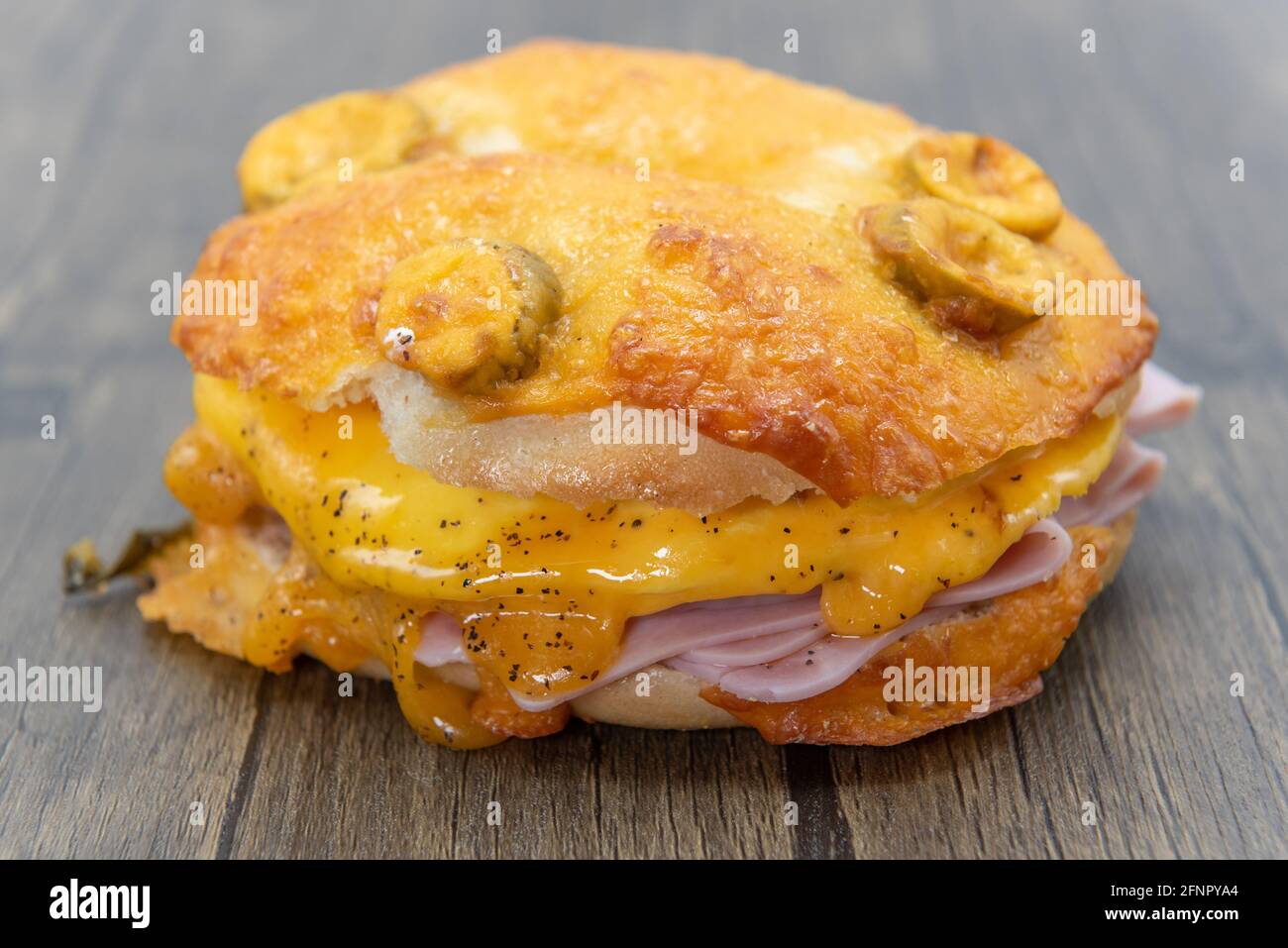 Melted cheese dripping over the stacks of sliced ham served inside a jalepeno breakfast bagel cut in half. Stock Photo
