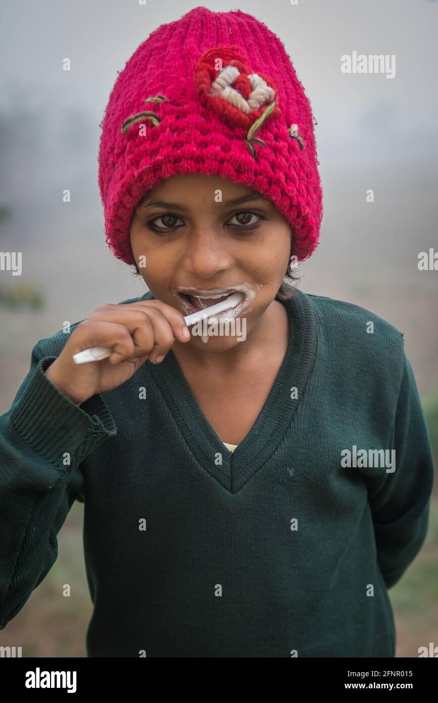 Uttar Pradesh, India. 05-11-2019.Portrait of a young indian girl wearing a red hat brushing her teeth after lunch before going back to her school acti Stock Photo