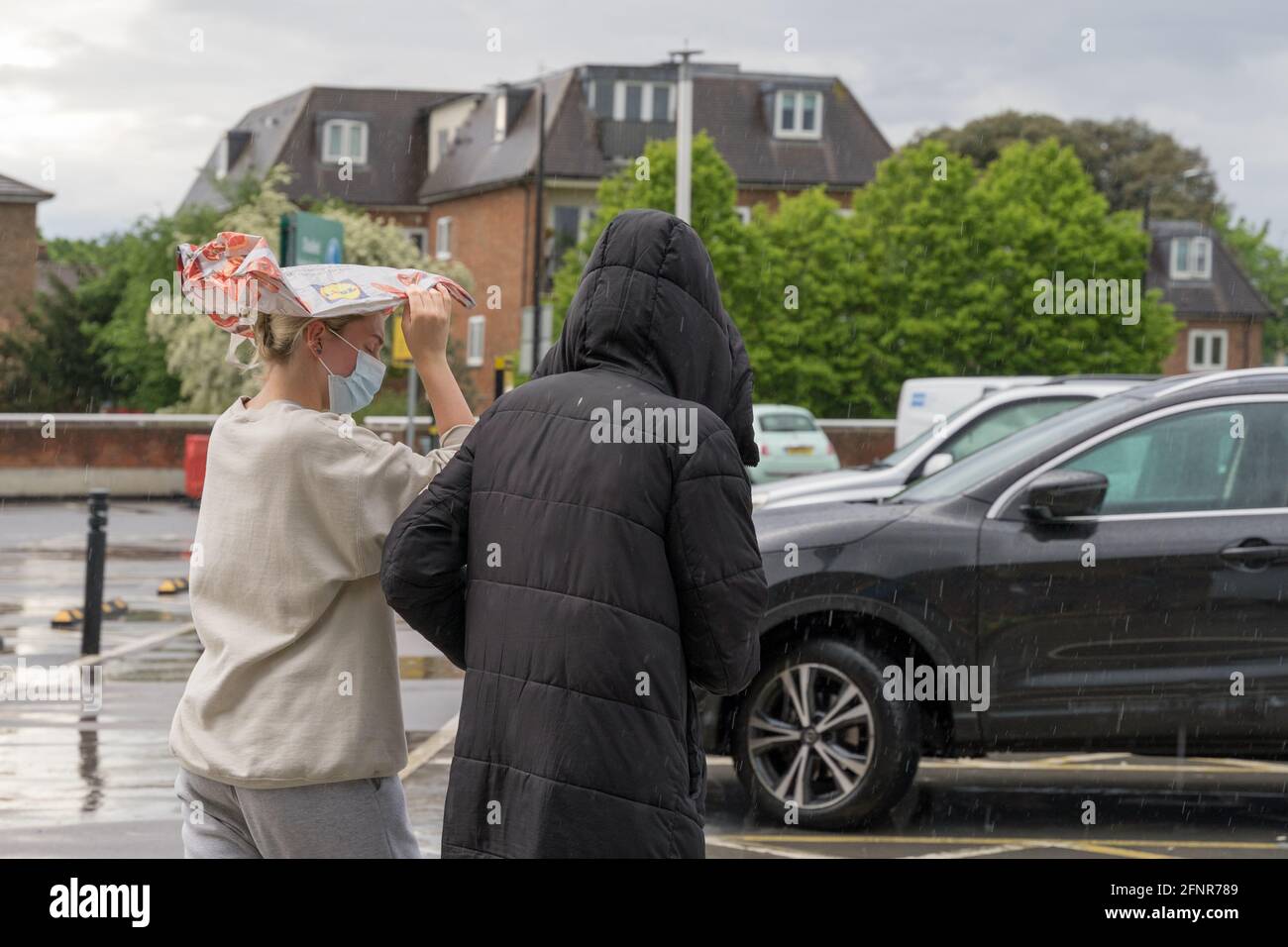shopper use shopping bag as umbrella to cover her hair in spring downpour , Morrisons, London Stock Photo