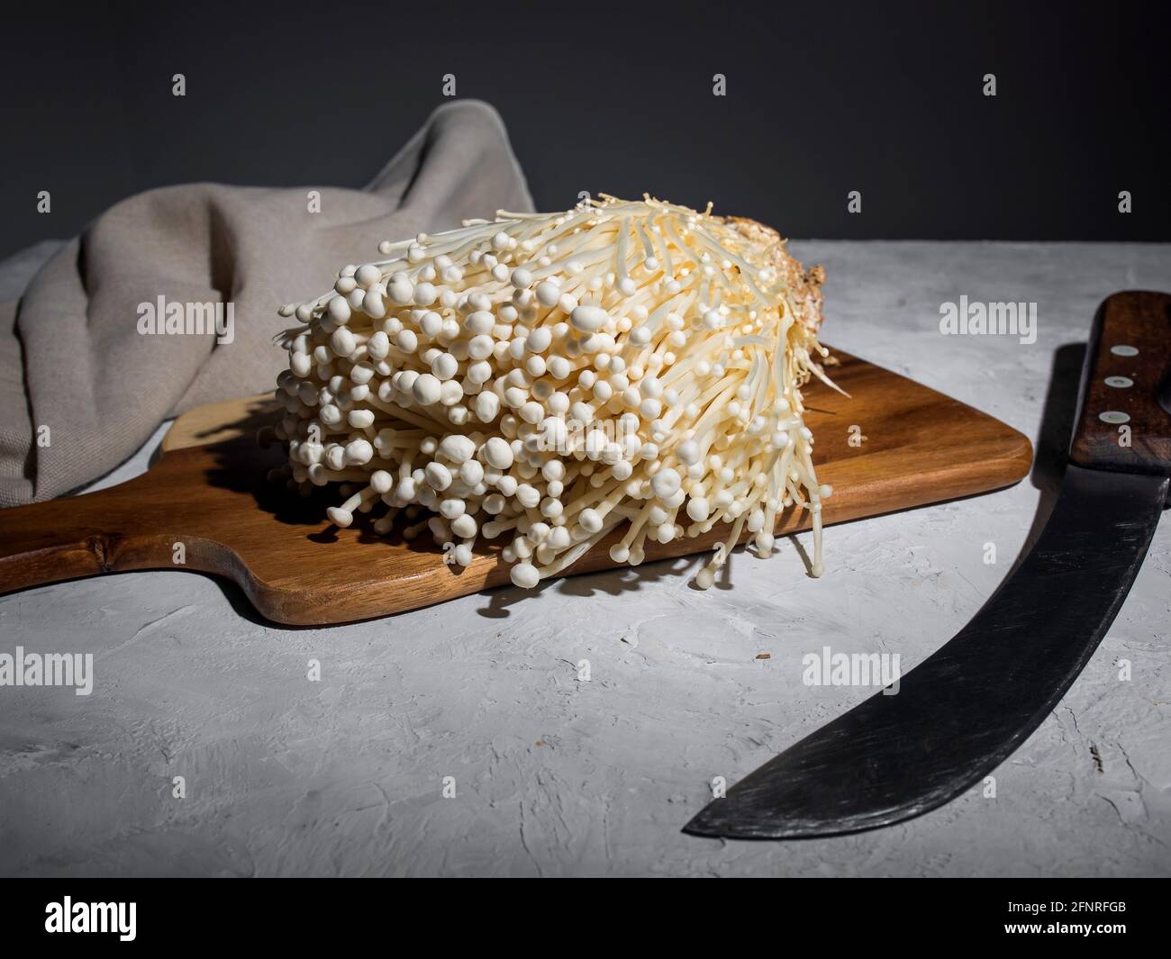 Fresh golden needle mushroom or enoki mushrooms, on wooden cutting board with vintage knife on gray concrete background Stock Photo