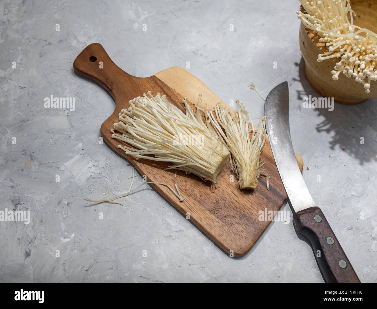 Fresh golden needle mushroom or enoki mushrooms, on wooden cutting board with vintage knife on gray concrete background Stock Photo