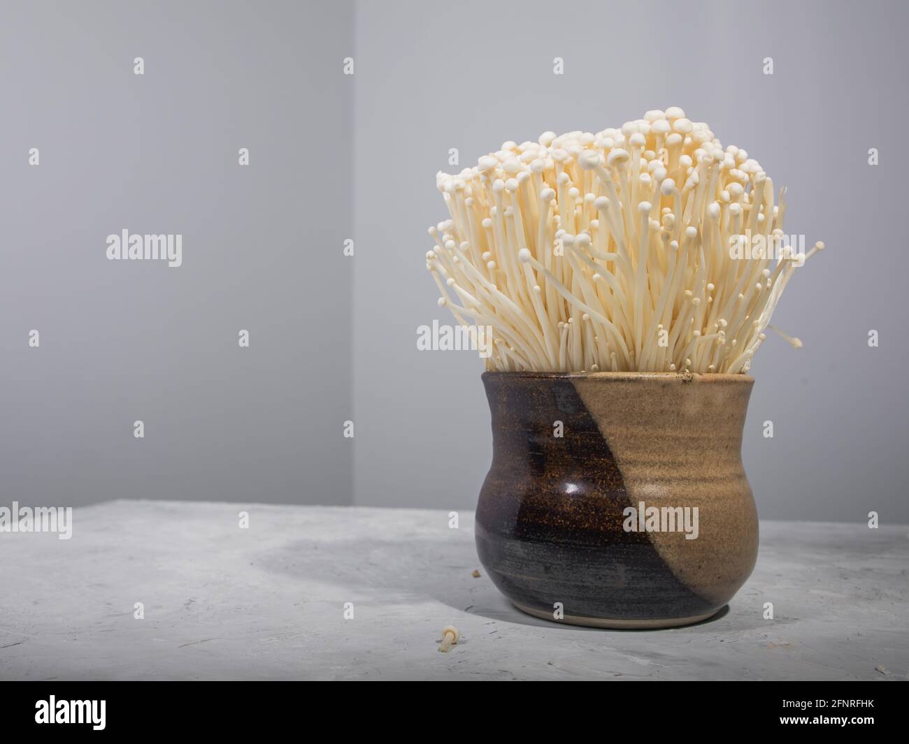 Enoki mushrooms in clay bowl on table Stock Photo