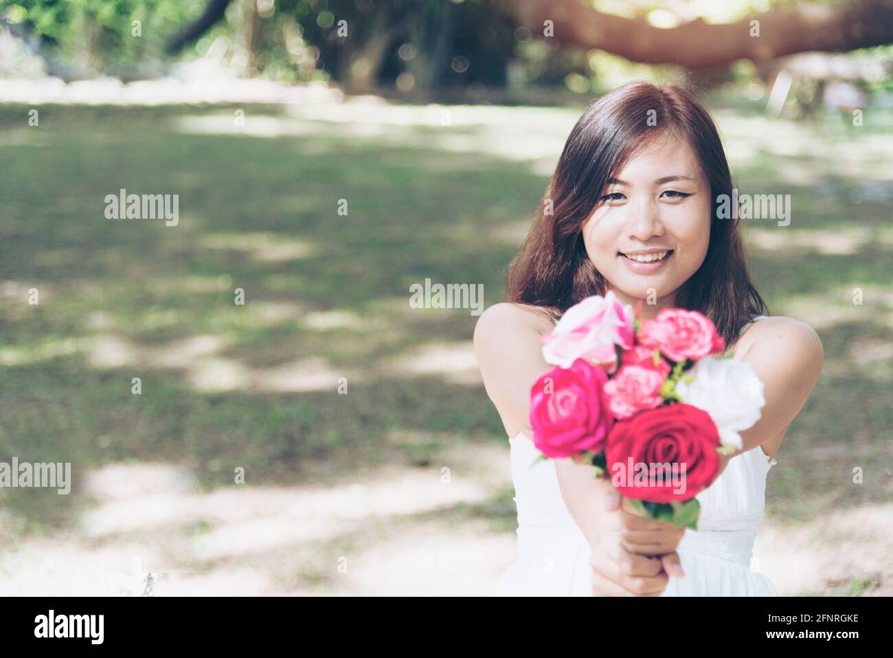 Cheerful beautiful woman holding roses bouquet and saying I am sorry in the park Stock Photo