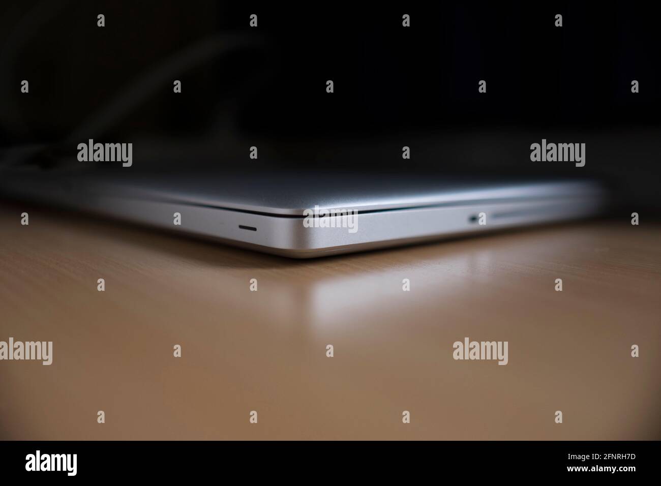 Closed aluminum laptop on a shiny wooden table. It is reflected in the table Stock Photo