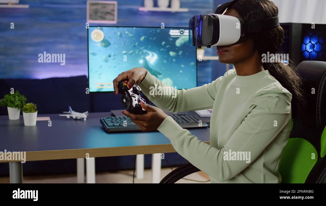 Black woman videogame player with vr goggles raising hands holding joystick after winning space shooter competition