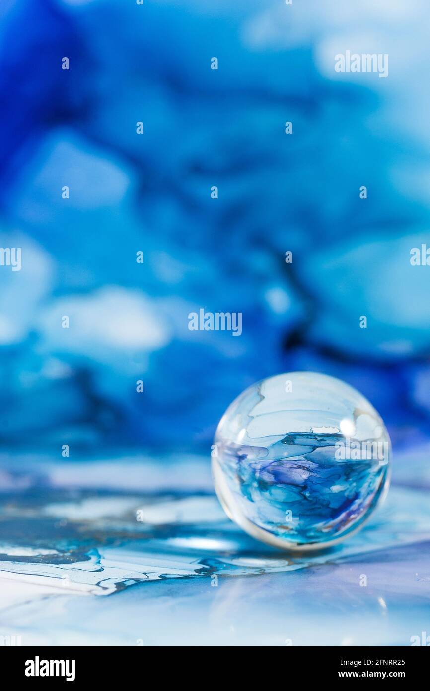 A transparent glass ball on an abstract blue background. The technique of alcoholic ink. Copy space. Stock Photo