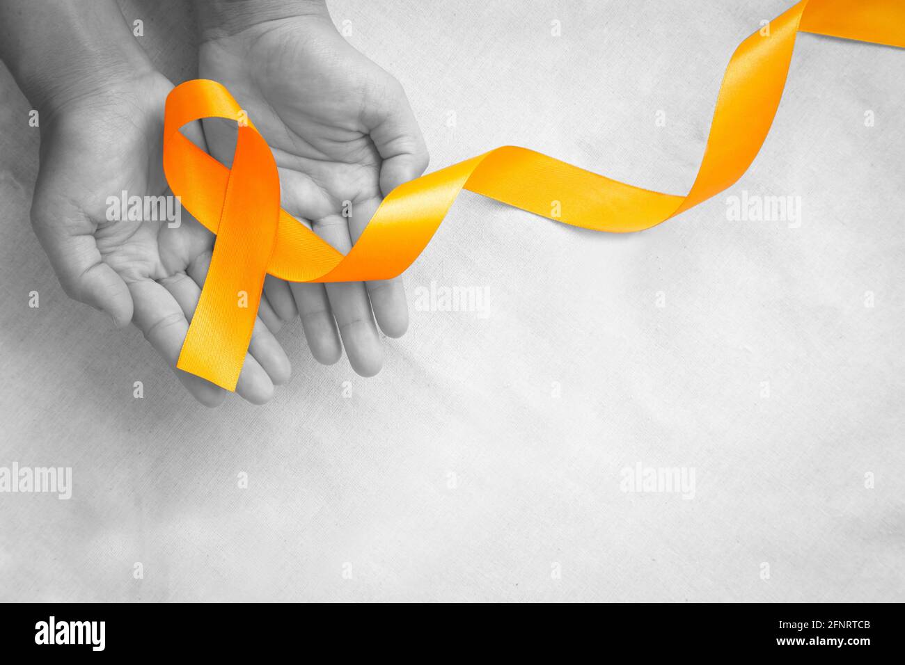 Hands holding orange color ribbon on white fabric with copy space. Kidney Cancer Awareness, Leukemia disease, Skin cancer awareness, World Cancer Day. Stock Photo