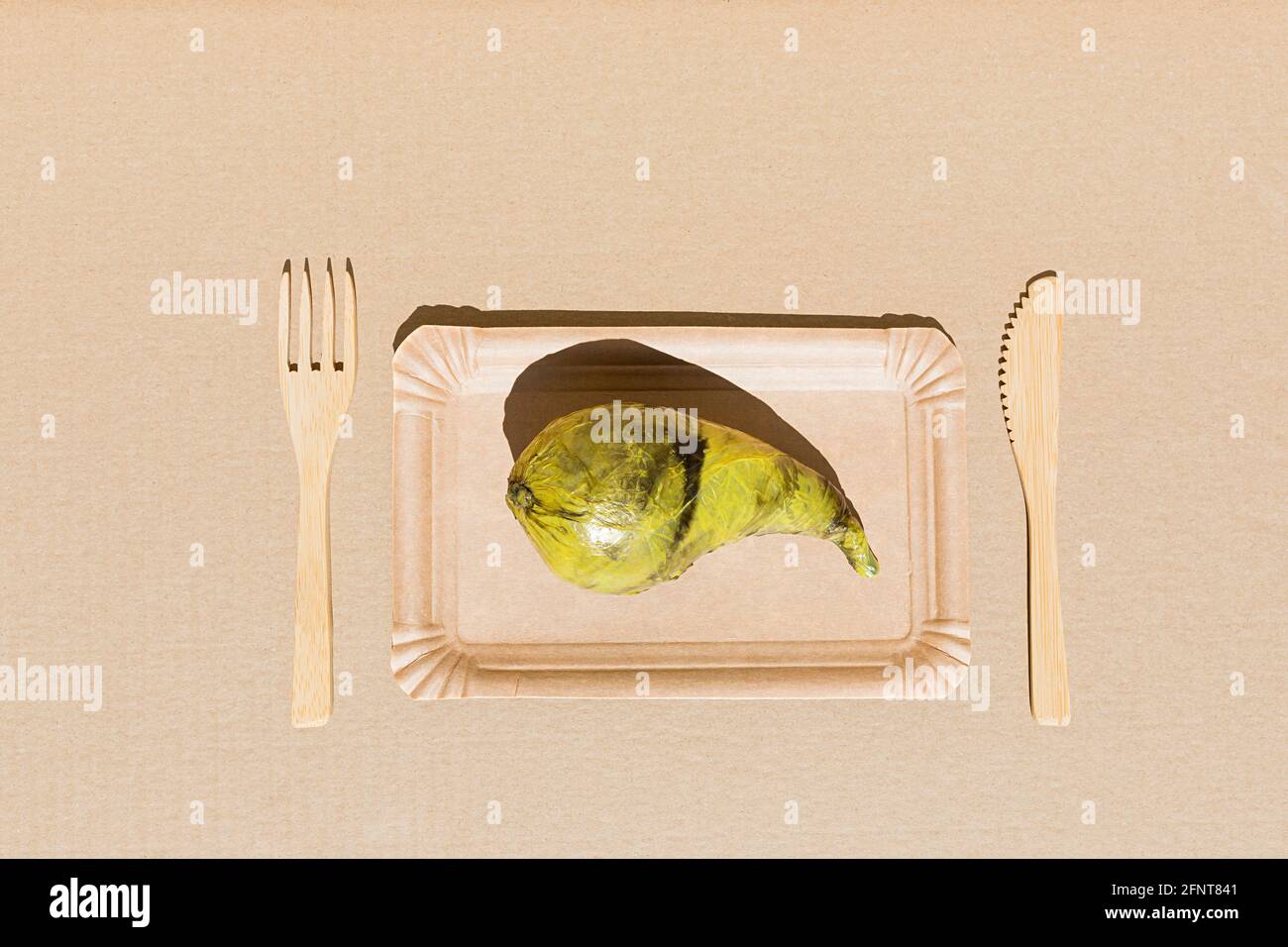 Pear wrapped in plastic on the beige paper background. Immature, tasteless or inedible food concept. Copy space. Flat lay. Stock Photo