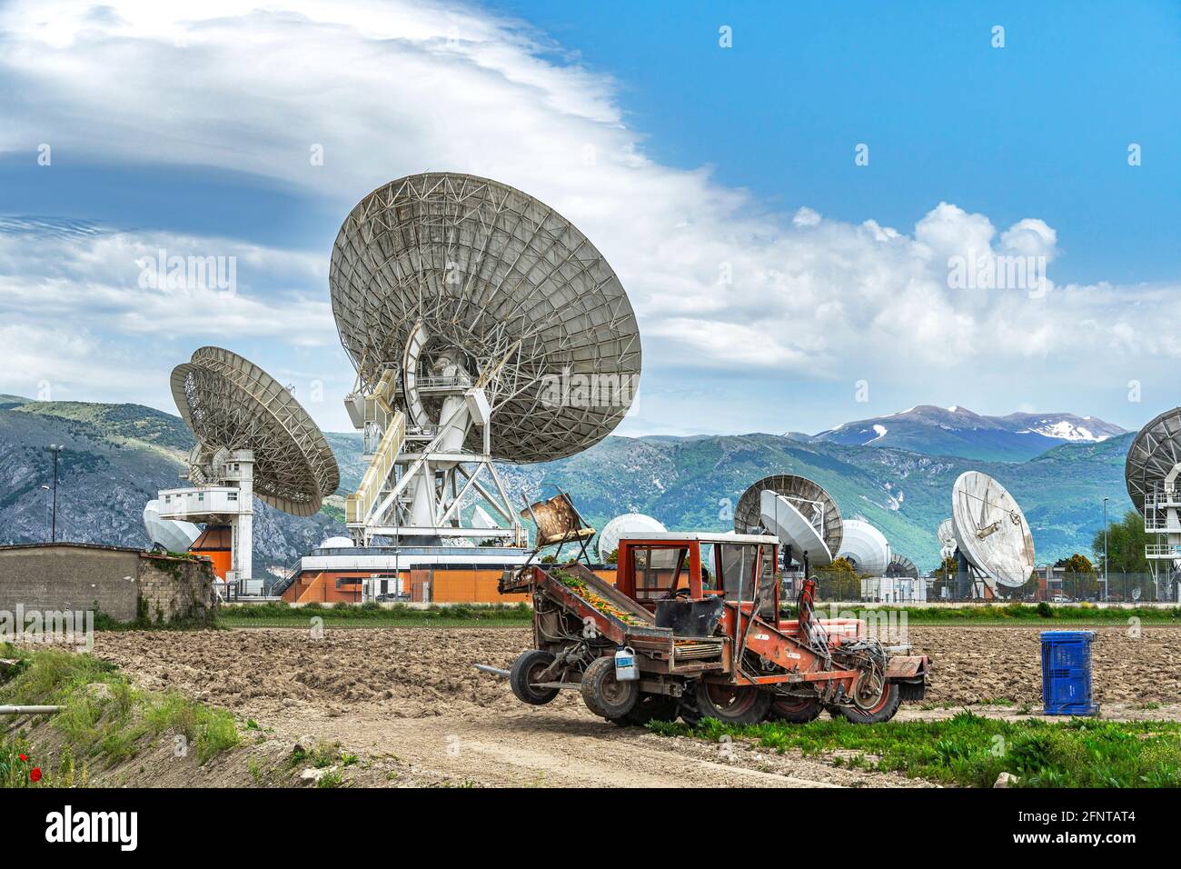 Contrasts of technologies in the Fucino plain. Satellite communication antennas and farm workers who collect carrots. Fucino, Abruzzo, Italy, Europe Stock Photo
