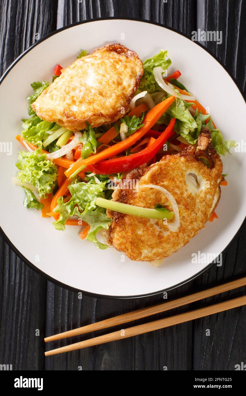 Yam khai dao fried egg spicy salad with vegetables and herbs is a Thai dish close up in the plate on the table. Vertical top view from above Stock Photo