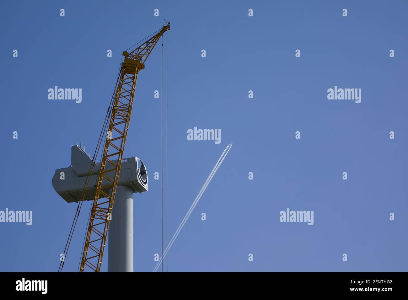An passenger aircraft is drawing contrails behind a wind turbine under construction Stock Photo