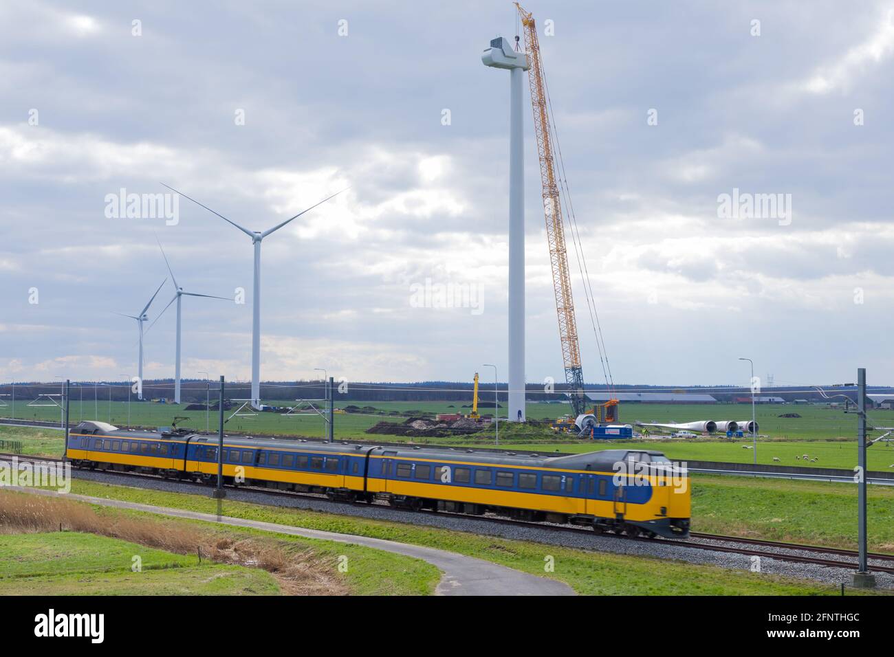 Construction of wind turbines along a railway with a train rushing by. Transport on renewable energy concept. Stock Photo