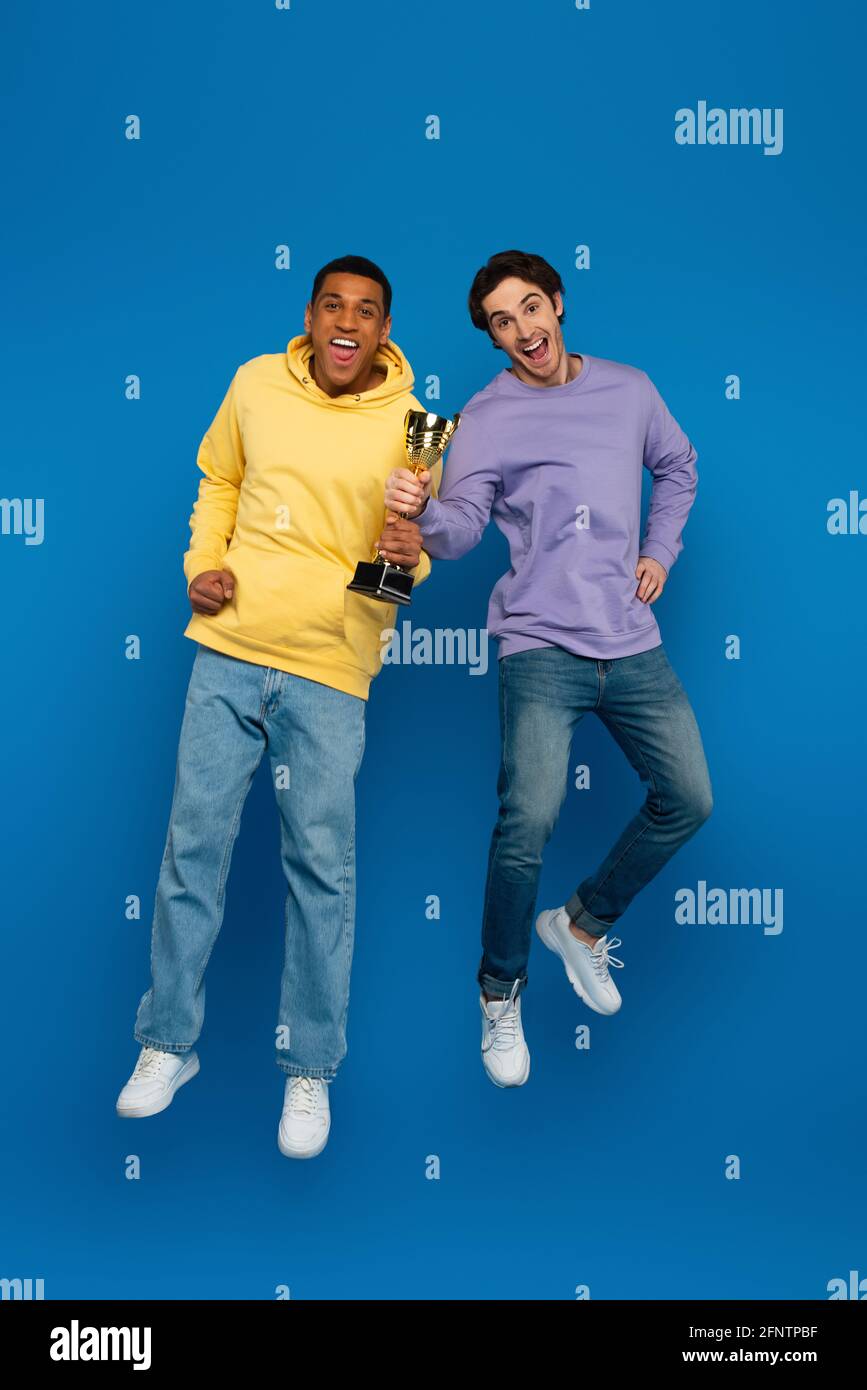 happy african american man with friend levitating and holding triumph cup  in hands on blue background Stock Photo