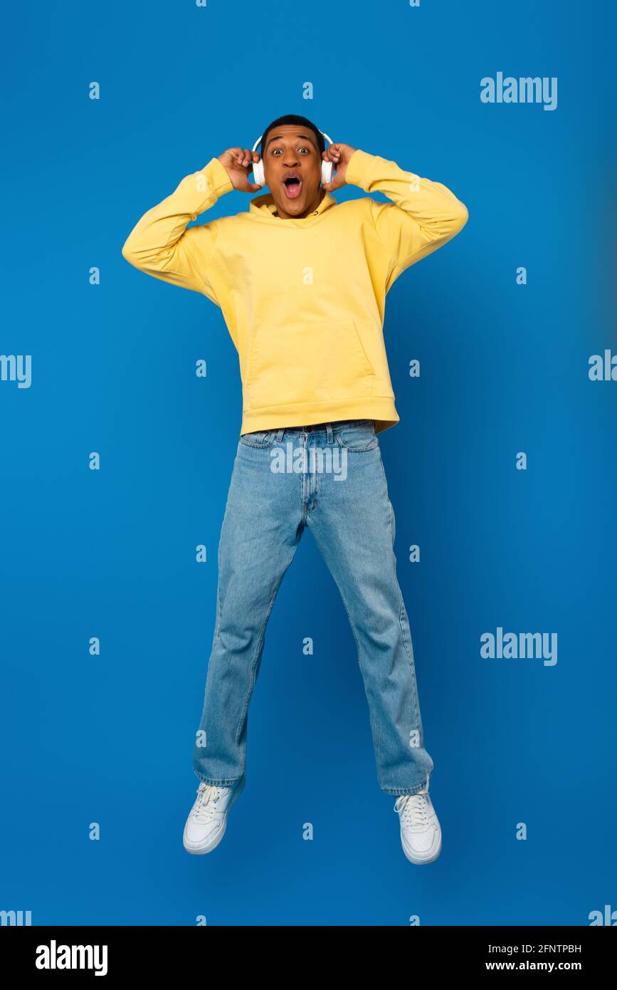 happy african american man jumping in headphones on blue background Stock Photo