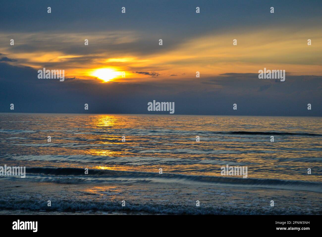 orange dramatic sunset on the sea beach with colorful sky and waves crushing on the shore Stock Photo