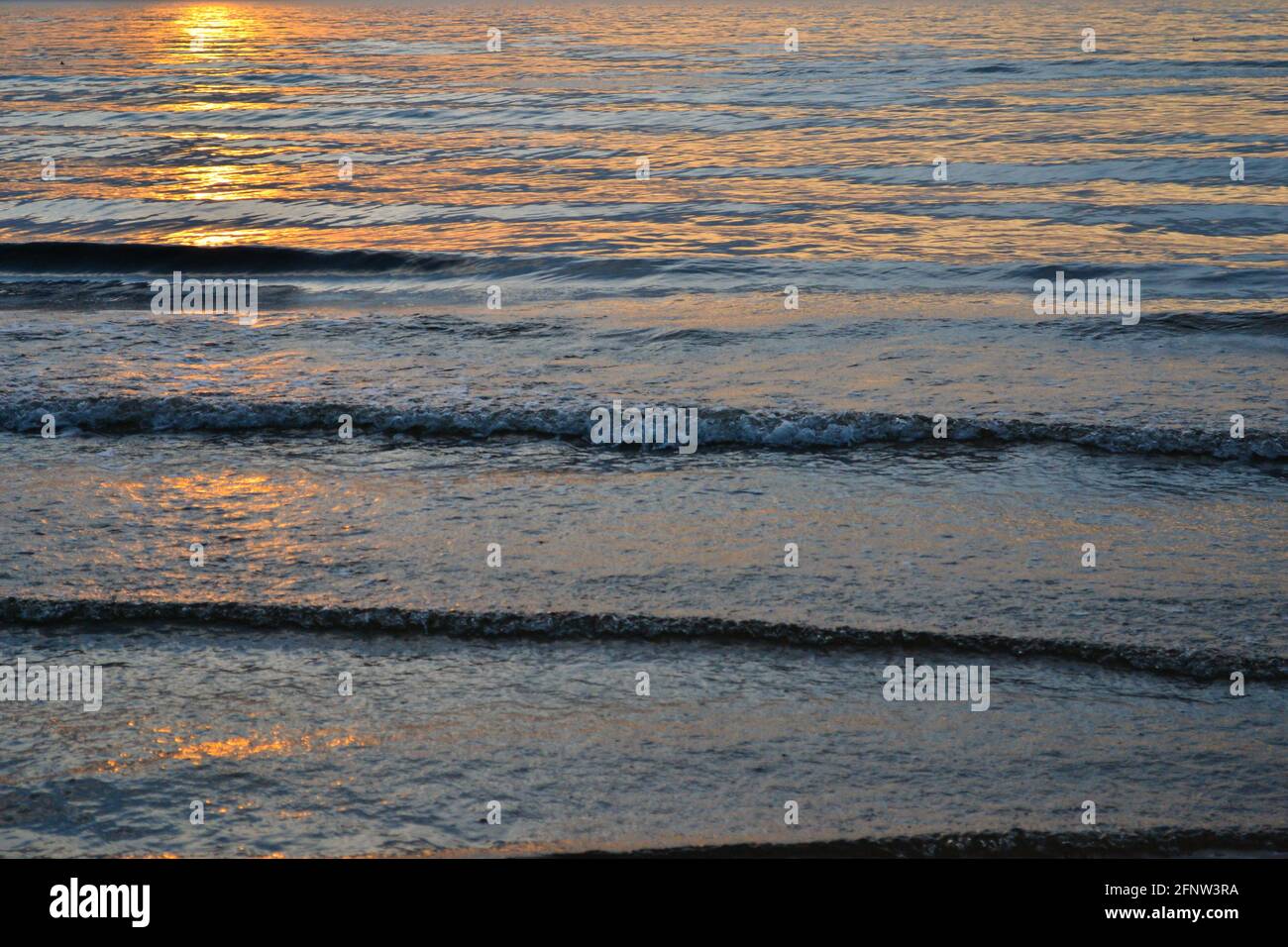 orange dramatic sunset on the sea beach with colorful sky and waves crushing on the shore Stock Photo