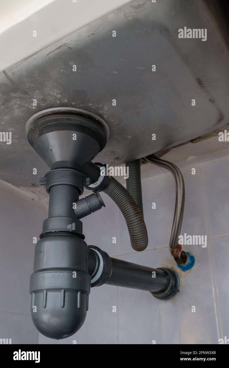 The drainage pipe system under the large sink in the house kitchen, near the metal pipe for use with the sink faucet, front view for the copy space. Stock Photo