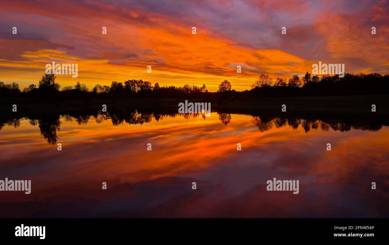 sunset at coast of the lake. Nature landscape. Nature in northern Europe. reflection, blue sky and orange sunlight. landscape during sunset. Stock Photo