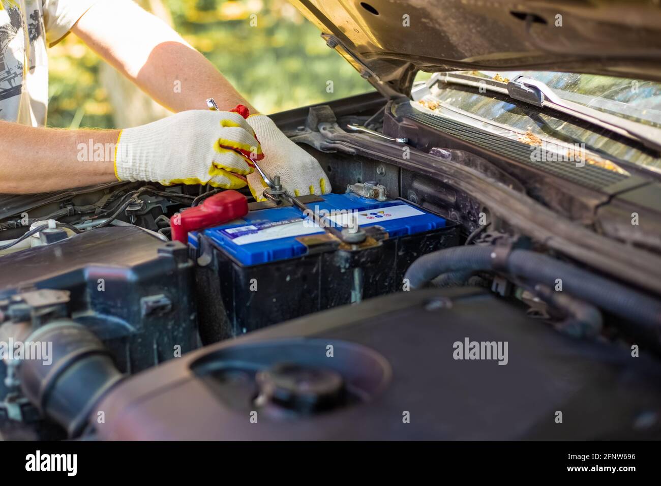 Man unscrews the battery mounting bolts with a wrench, installing and replacing spare parts on a car. Stock Photo