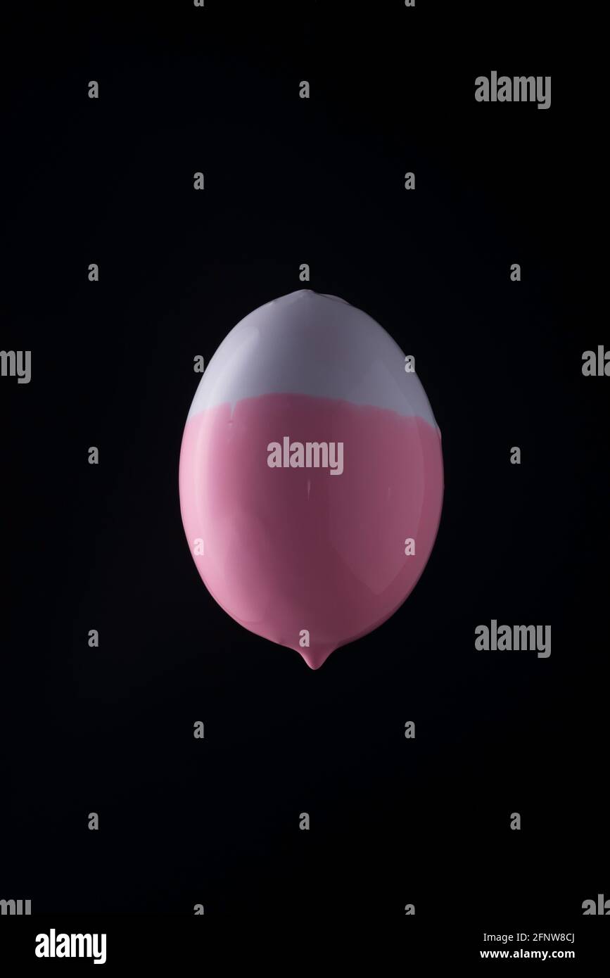 white-pink paint dripping down half an Easter egg. On a blue background Stock Photo