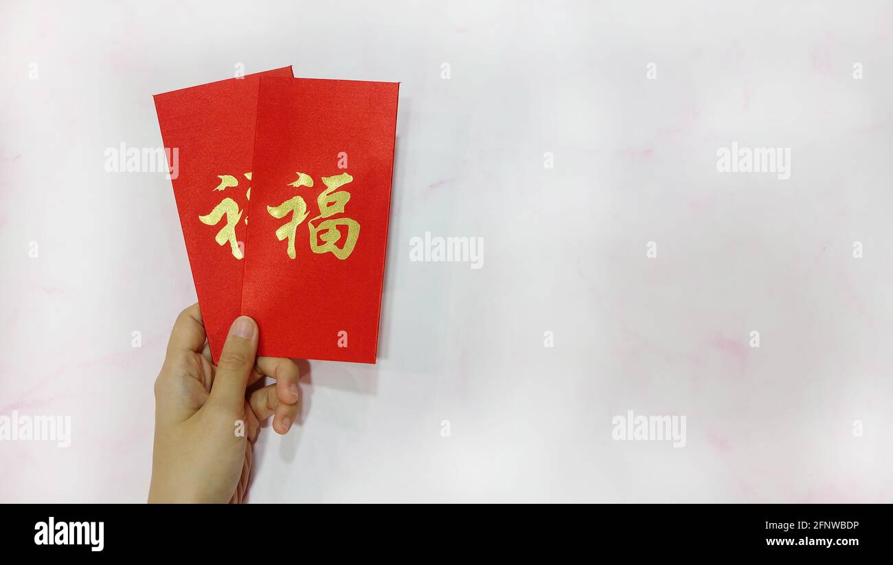 A hand holding two angpau, which are red packets with money inside, given as blessings in Chinese culture, especially during Chinese New Year. Stock Photo