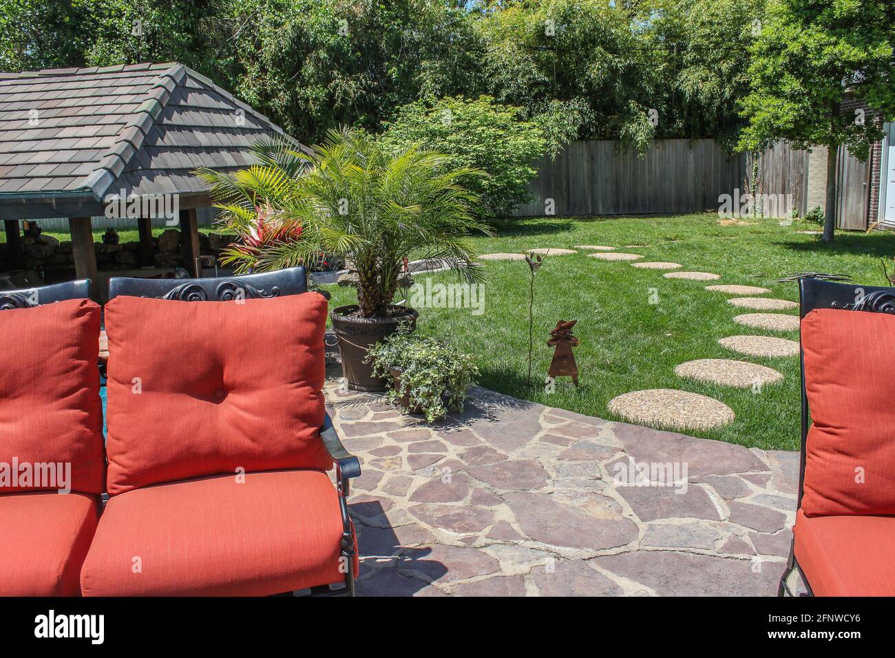 Backyard garden with patio and stepping stones to covered outdoor living area - orange cushioned lawn furniture in foreground with wooden privacy fenc Stock Photo