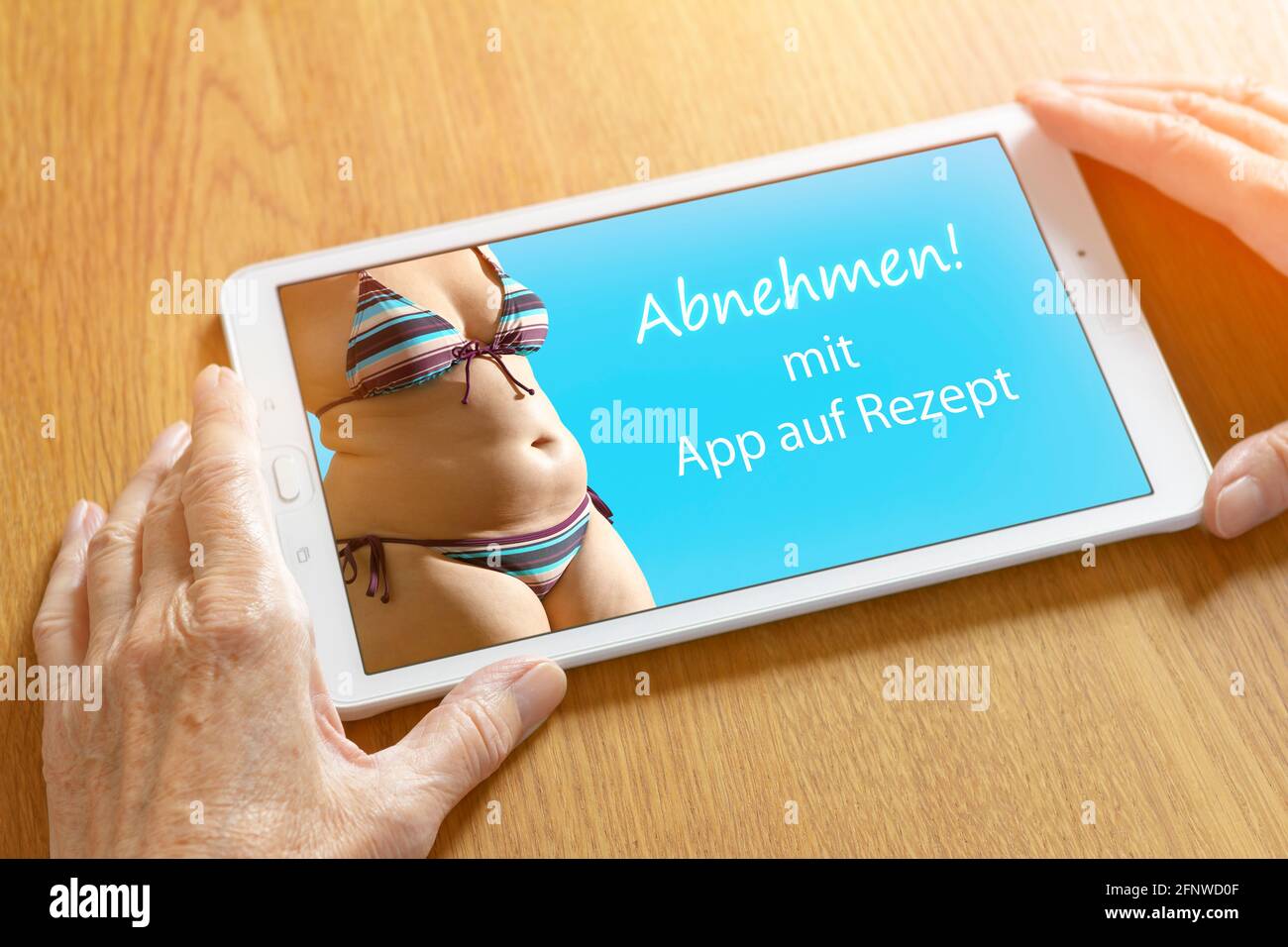 Hands of an older woman with a tablet computer showing a fat woman in bikini and the german text: Abnehmen mit App auf Rezept, translation: slimming w Stock Photo