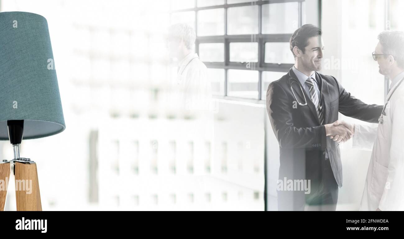 Composition of two smiling male doctors shaking hands in corridor with double exposure Stock Photo
