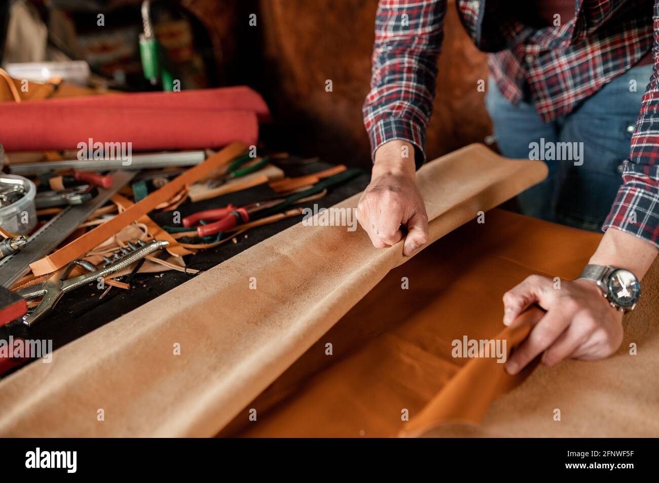 Unrecognizable craftsman working with piece of genuine leather in his workshop. Stock Photo