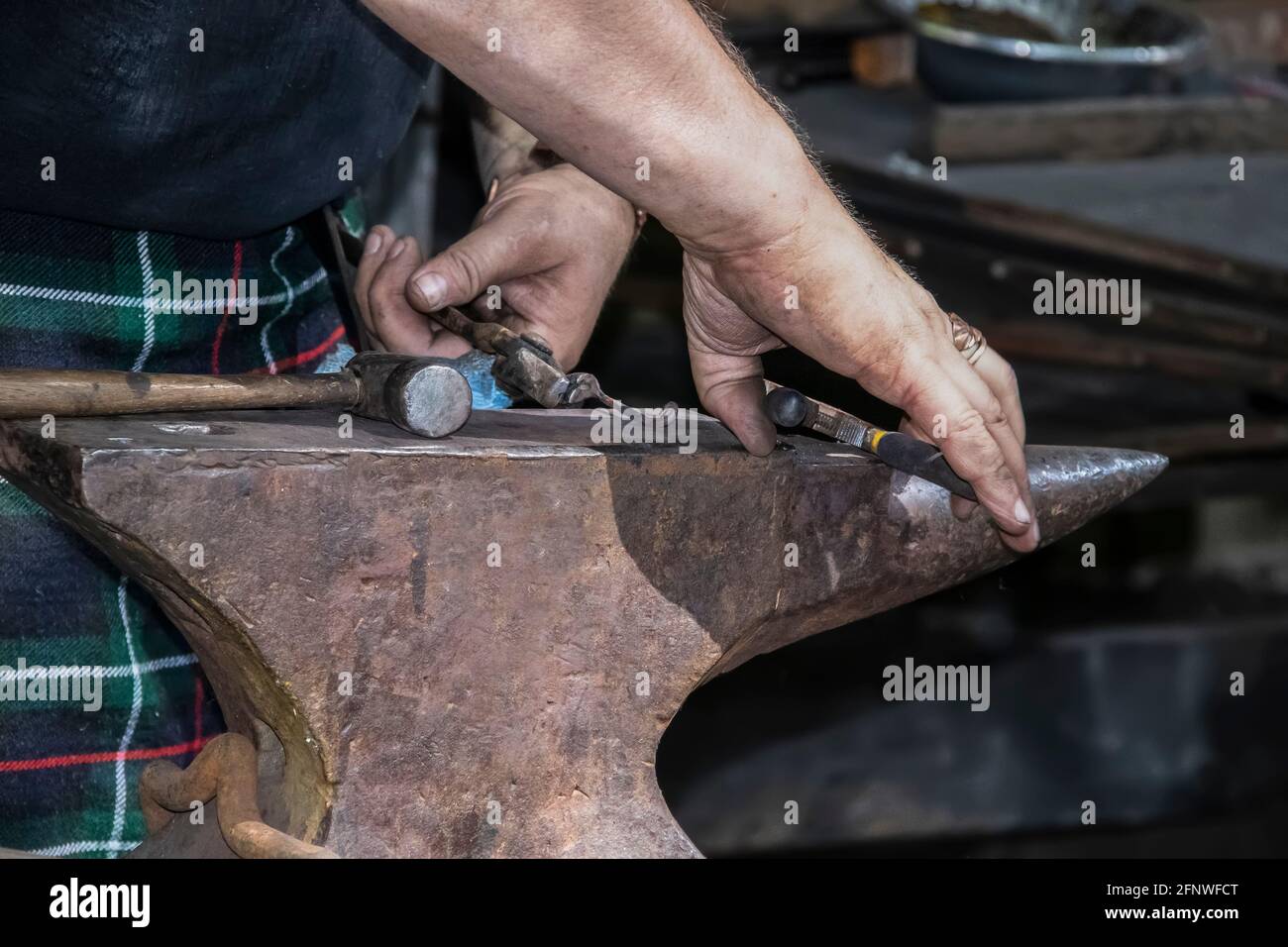 Blacksmith in kilts dirty hands - close-up - working metal on an anvil - selective focus Stock Photo
