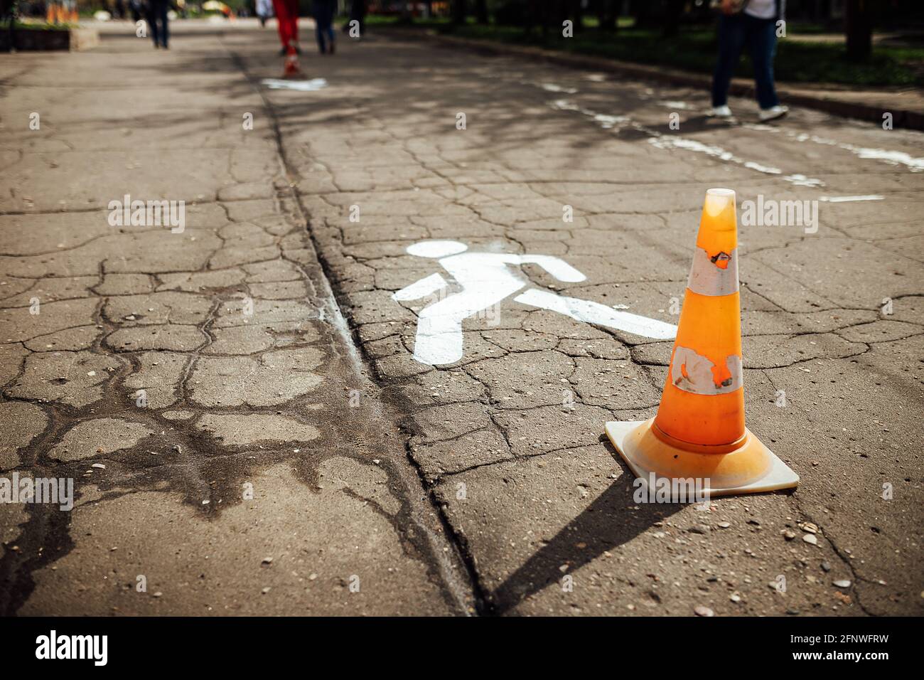 fresh marking of the pedestrian path on the asphalt. the workers painted the symbol of the man with white paint. orange cone warns of roadworks Stock Photo