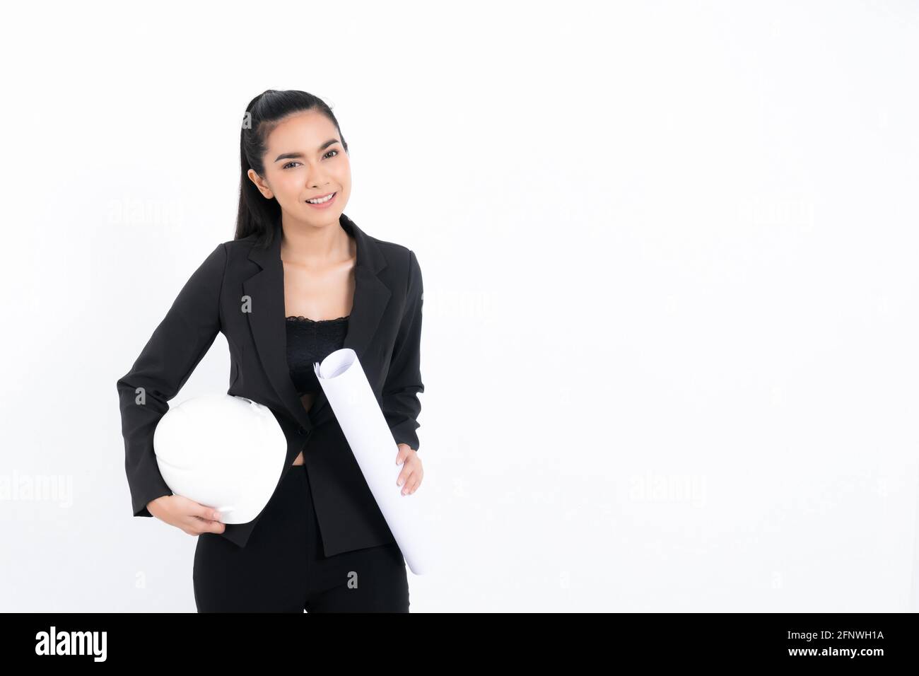 Portrait young engineer woman wearing black suit holding blueprint and white safety-helmet in shot studio isolated on white background. Stock Photo