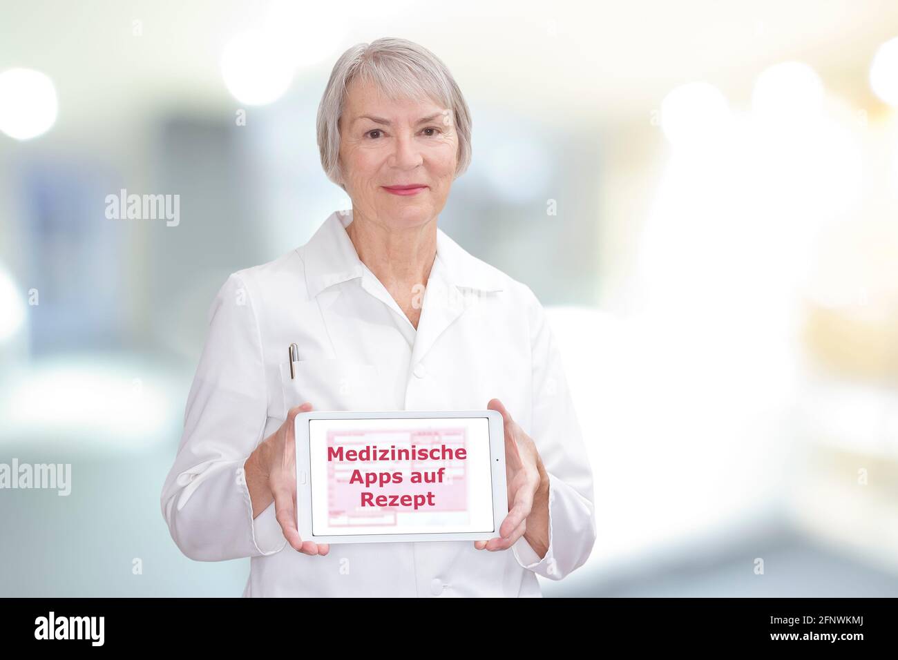 Senior doctor showing a tablet computer with the german text: Medizinische Apps auf Rezept. Translation: medicinal apps on prescription. Stock Photo