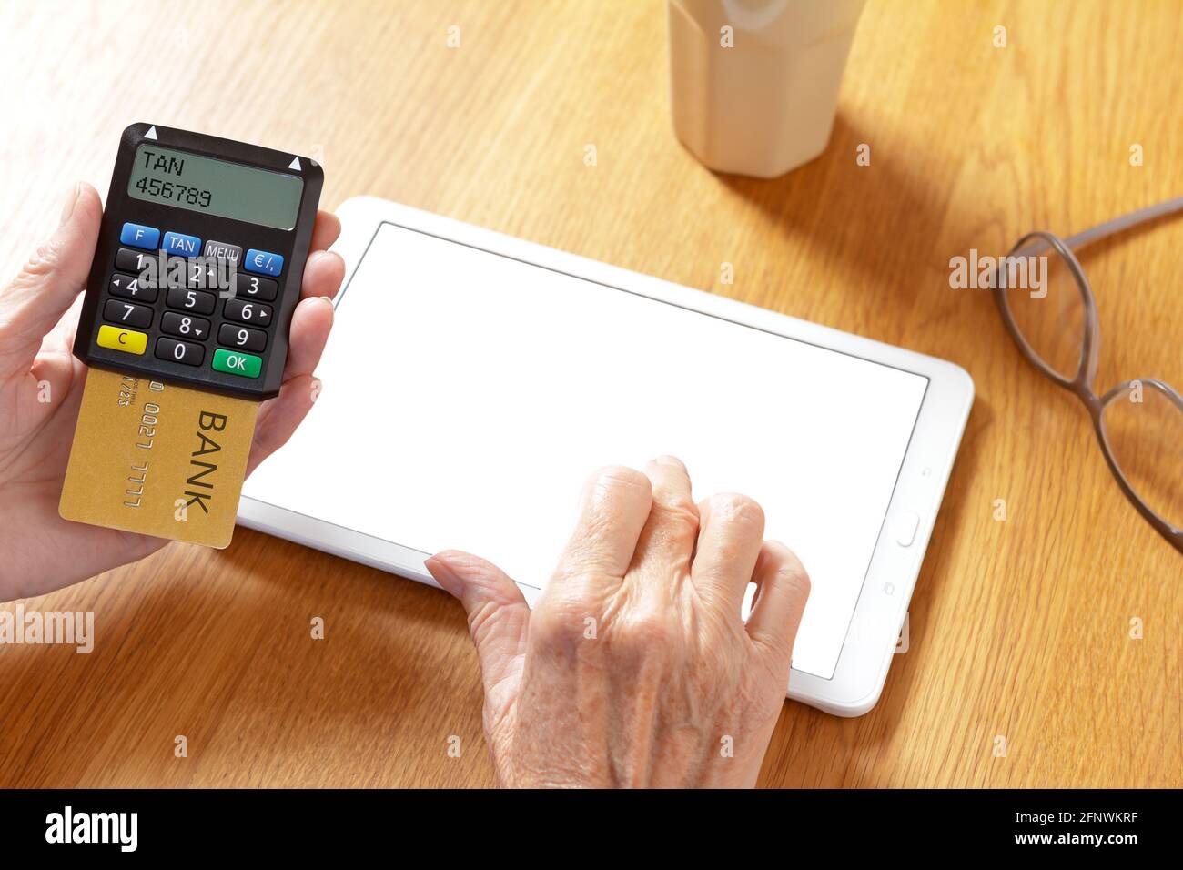 Hands of senior woman with a tablet pc and a confirmation code generator to log into the bank account, blank screen, mockup. Stock Photo