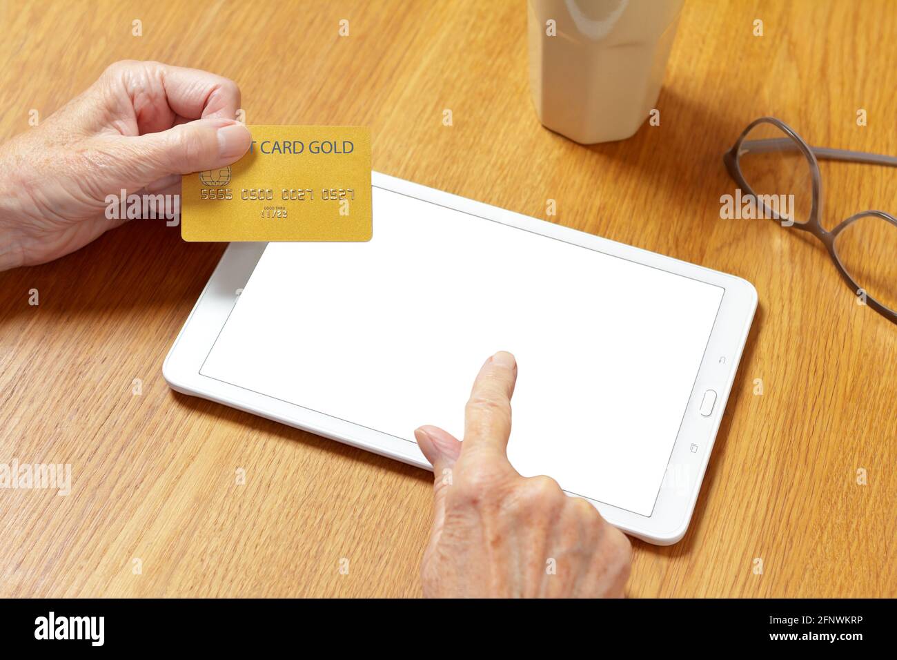 Hands of senior woman touching the screen of a tablet computer to pay with a credit card, online shopping mock up. Stock Photo