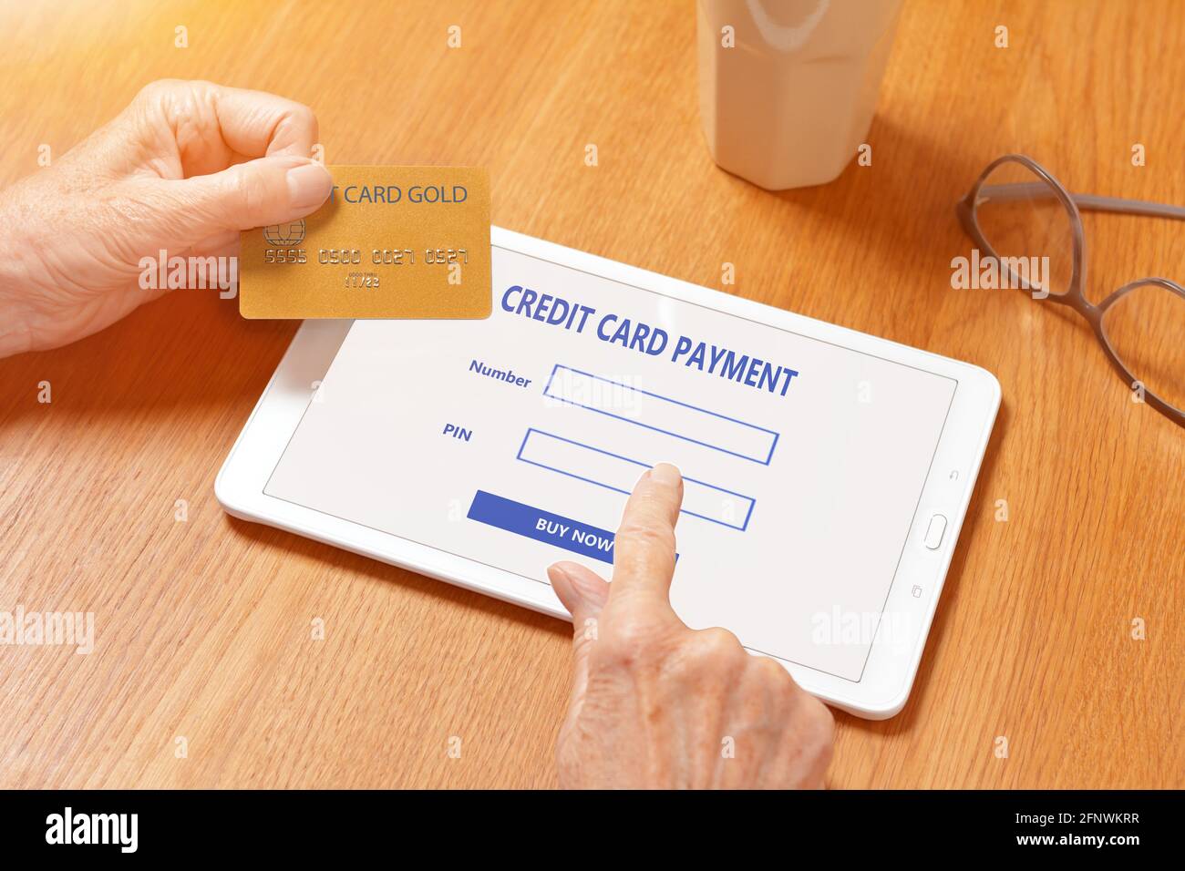 Hands of senior woman touching the screen of a tablet computer to pay with a credit card for something bought on the internet. Stock Photo