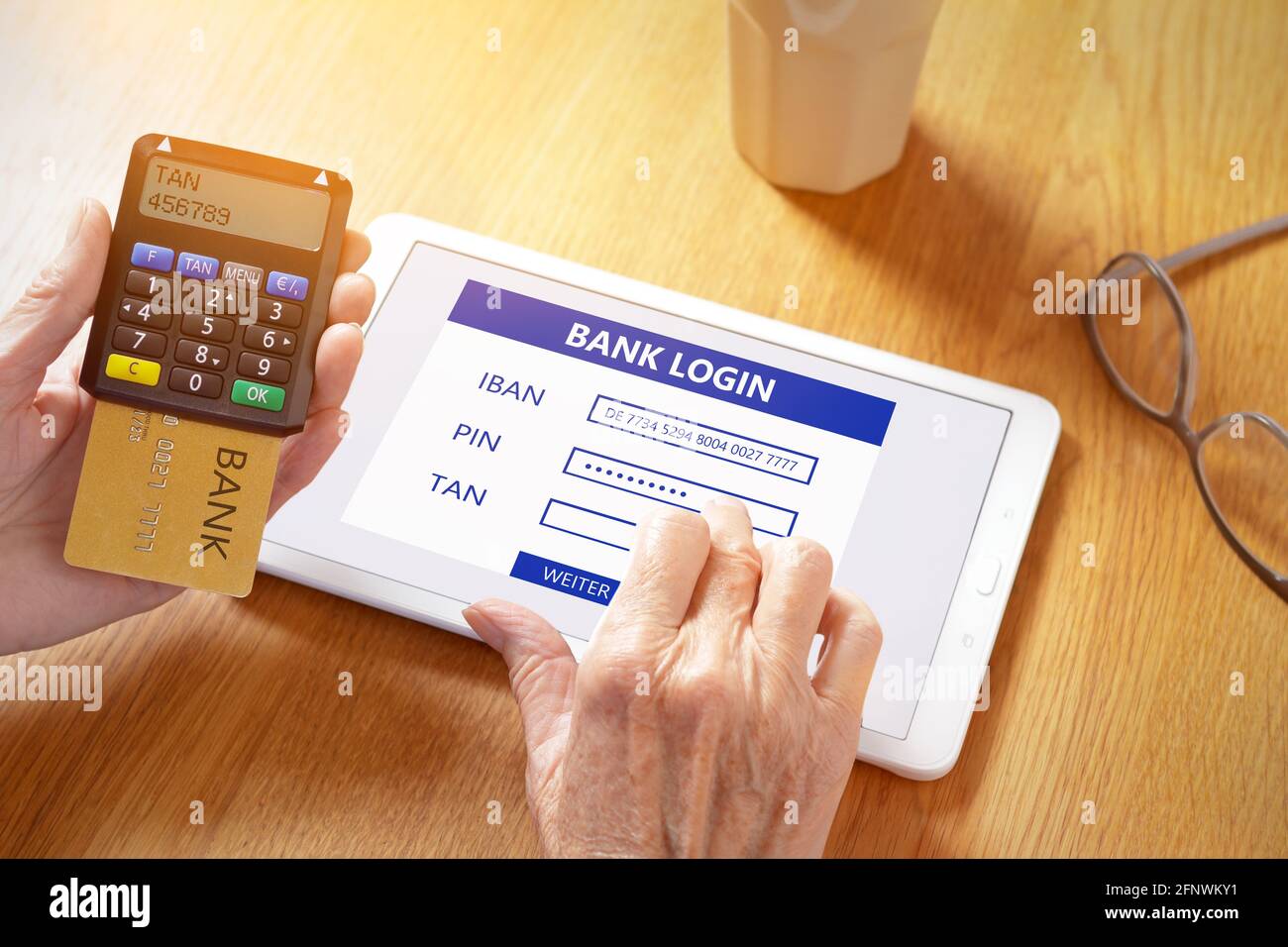 Hands of senior woman with a tablet computer and a confirmation code generator for online log in to the bank account. Stock Photo