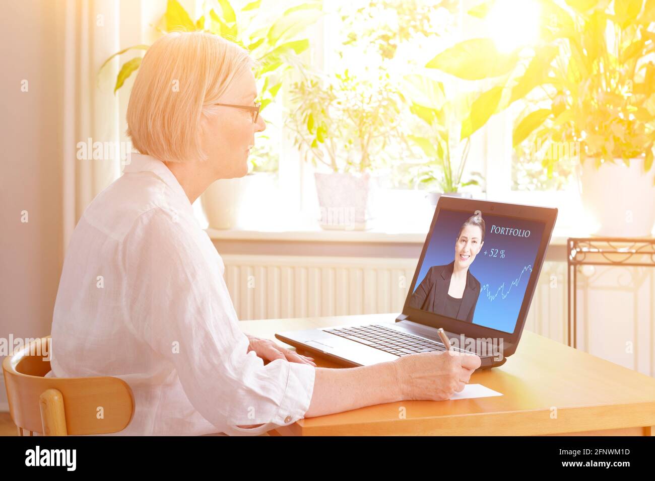 Senior woman at home in front of her laptop watching an online video of a female financial consultant. Stock Photo