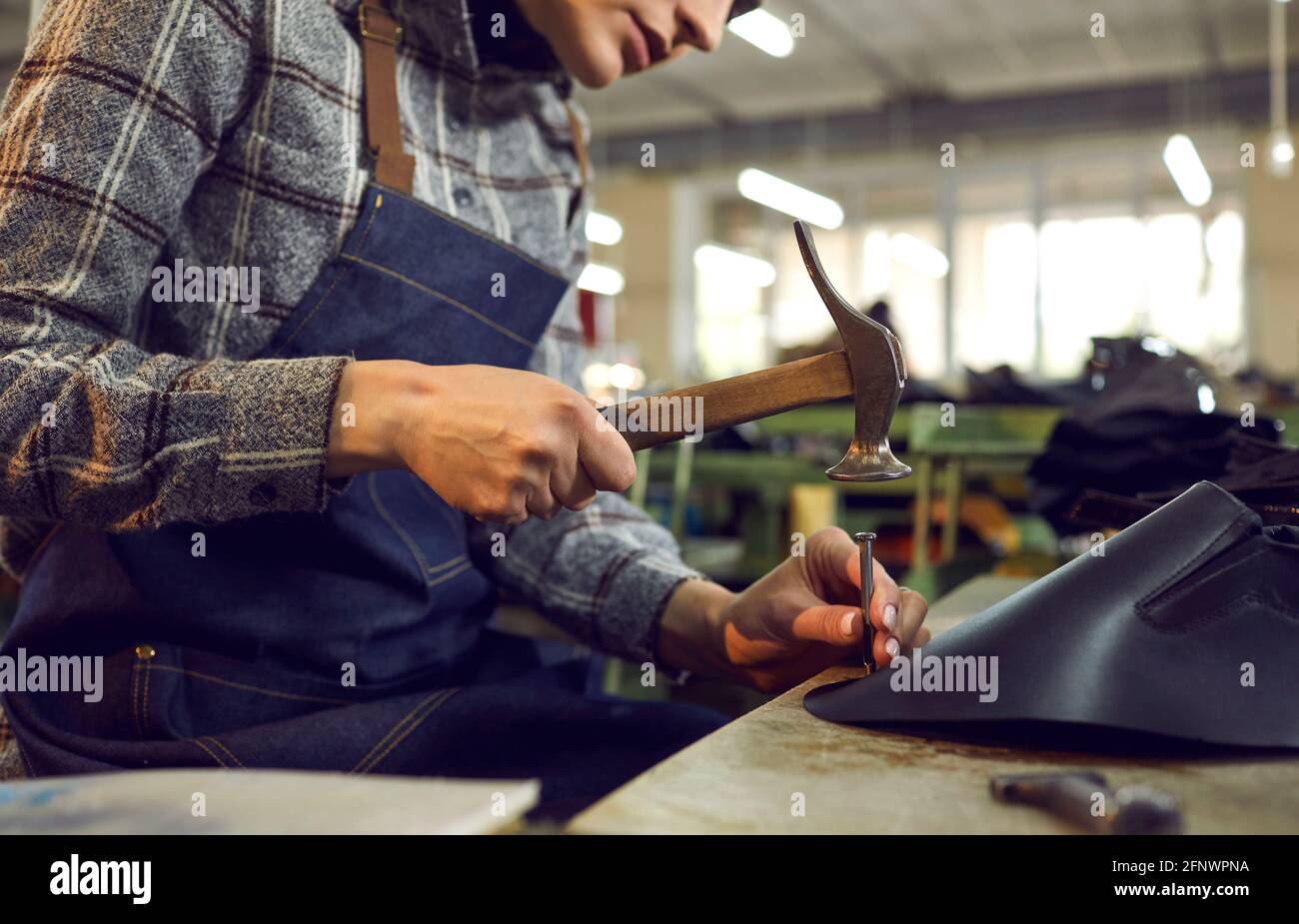 Shoe factory worker sitting at table and using hammer to make